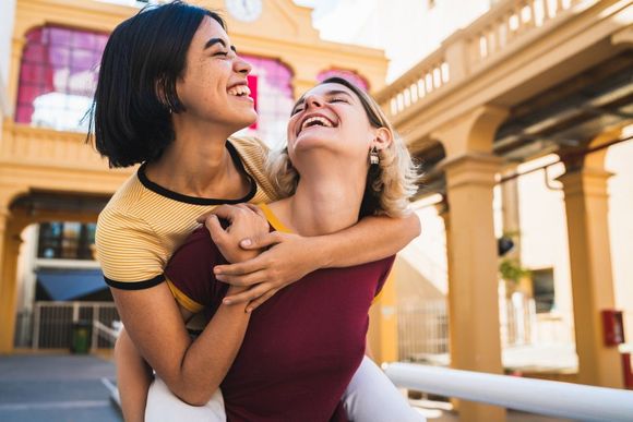 Two women are hugging each other and laughing in front of a building.