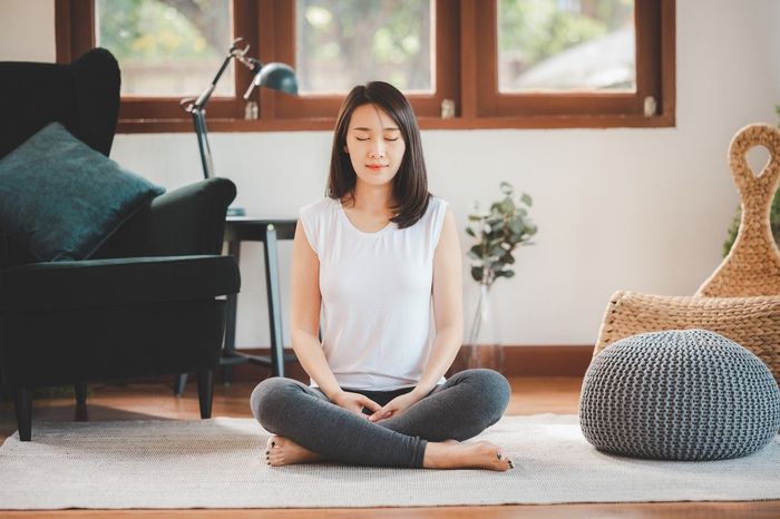 A woman is sitting in a lotus position on the floor in a living room.