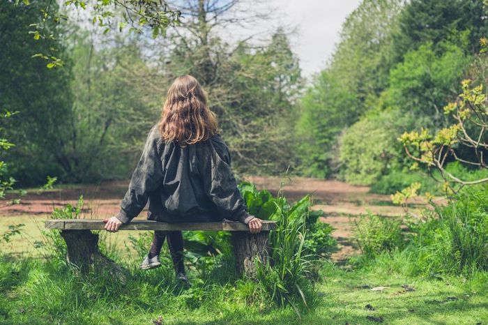 A woman is sitting on a bench in the middle of a forest.