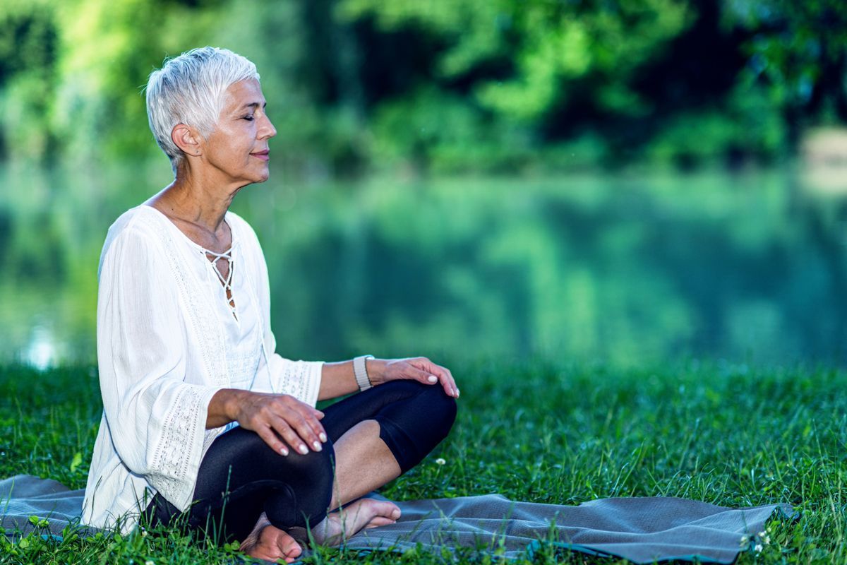 Older woman meditating in nature, practicing mindfulness and calm reflection.