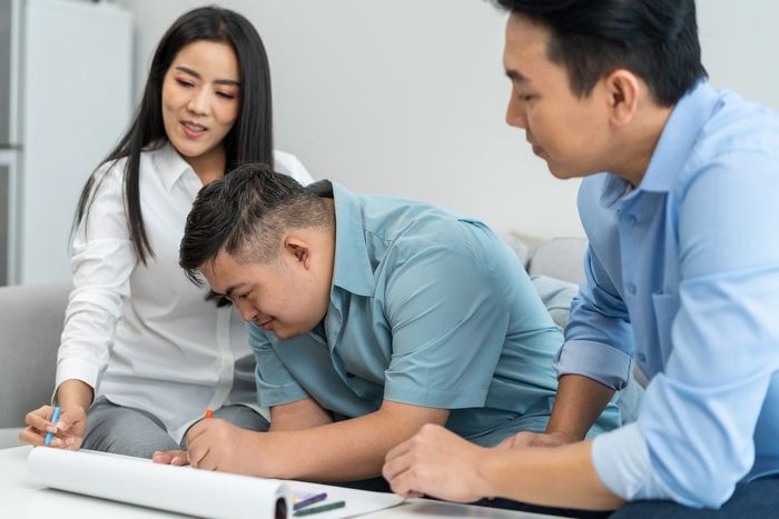 A group of people are sitting around a table looking at a laptop.
