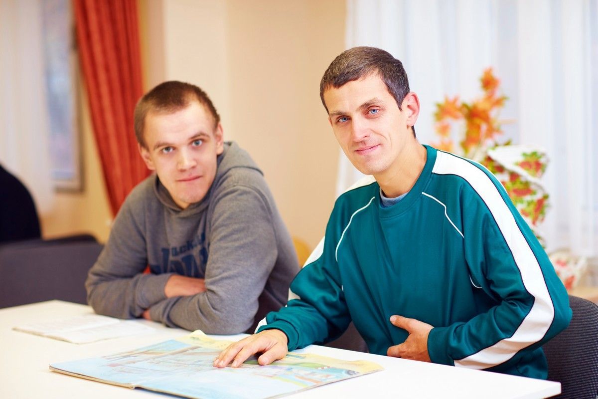 Two men sitting at a table, one gesturing toward a map.