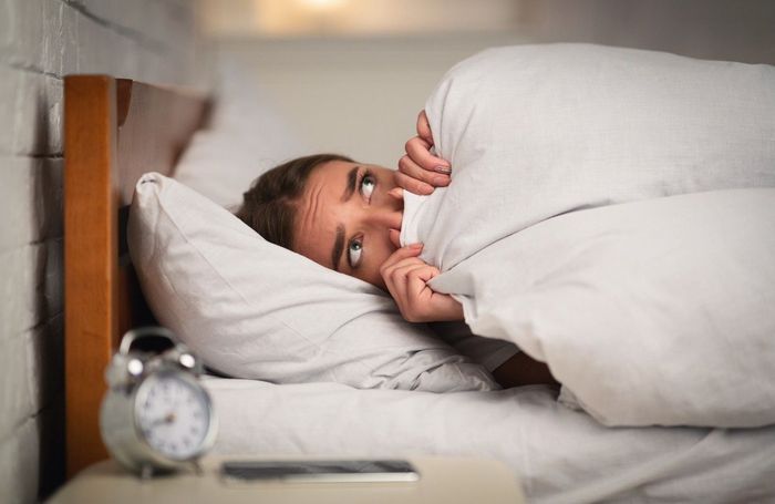 A woman is laying in bed covering her face with a pillow.