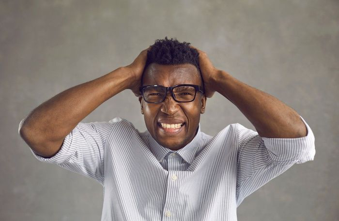 A man with glasses is holding his head in pain.