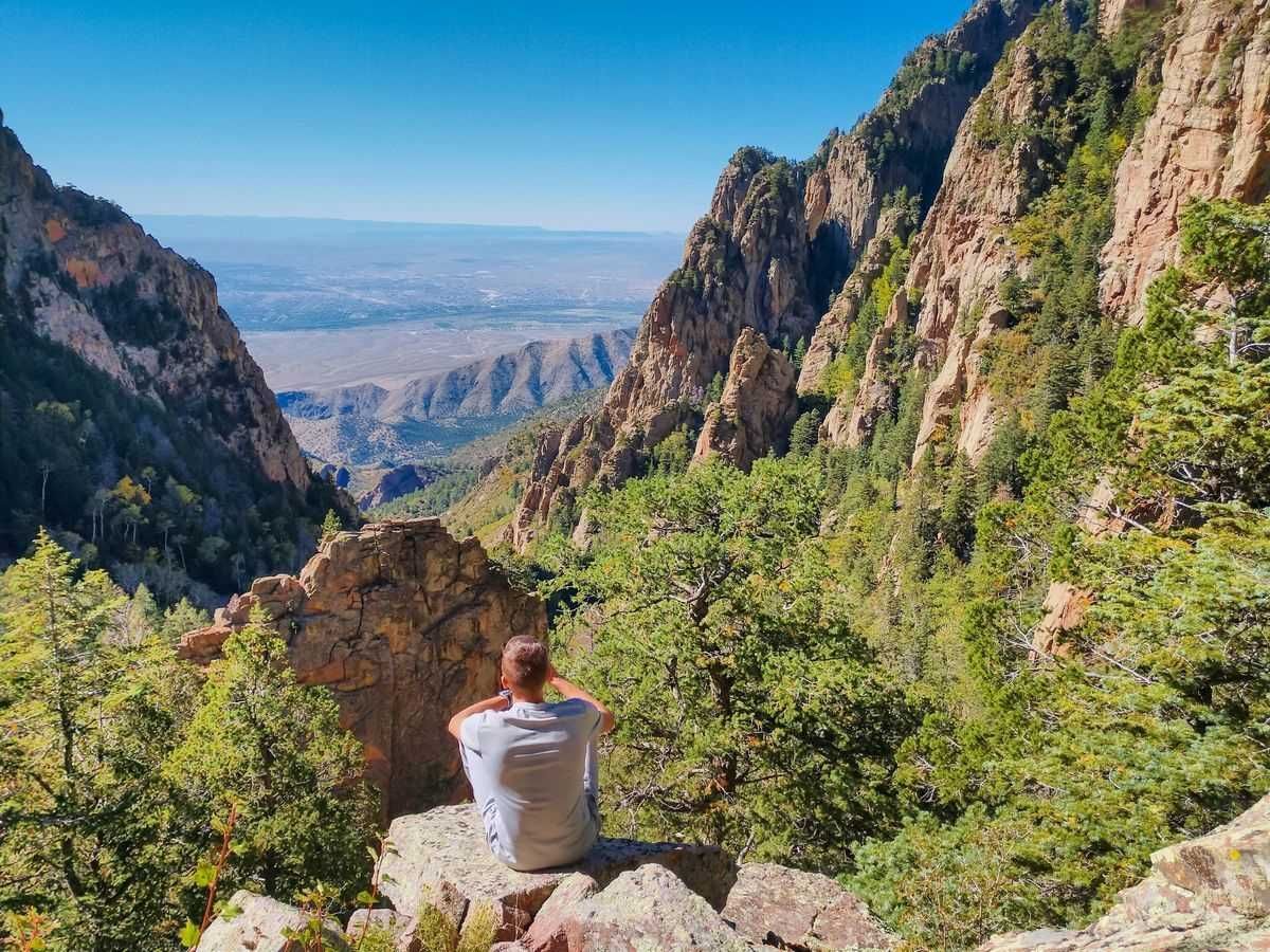 Man sitting quietly on a rock overlooking the Sandia Mountains in Albuquerque, symbolizing meditation and mindfulness.