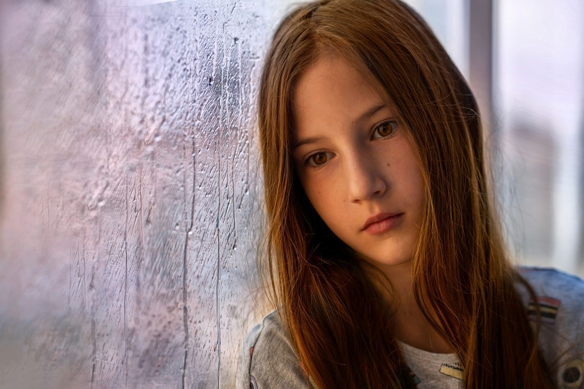 Teen girl looking out a rainy window, representing youth loneliness and mental health support in Alb