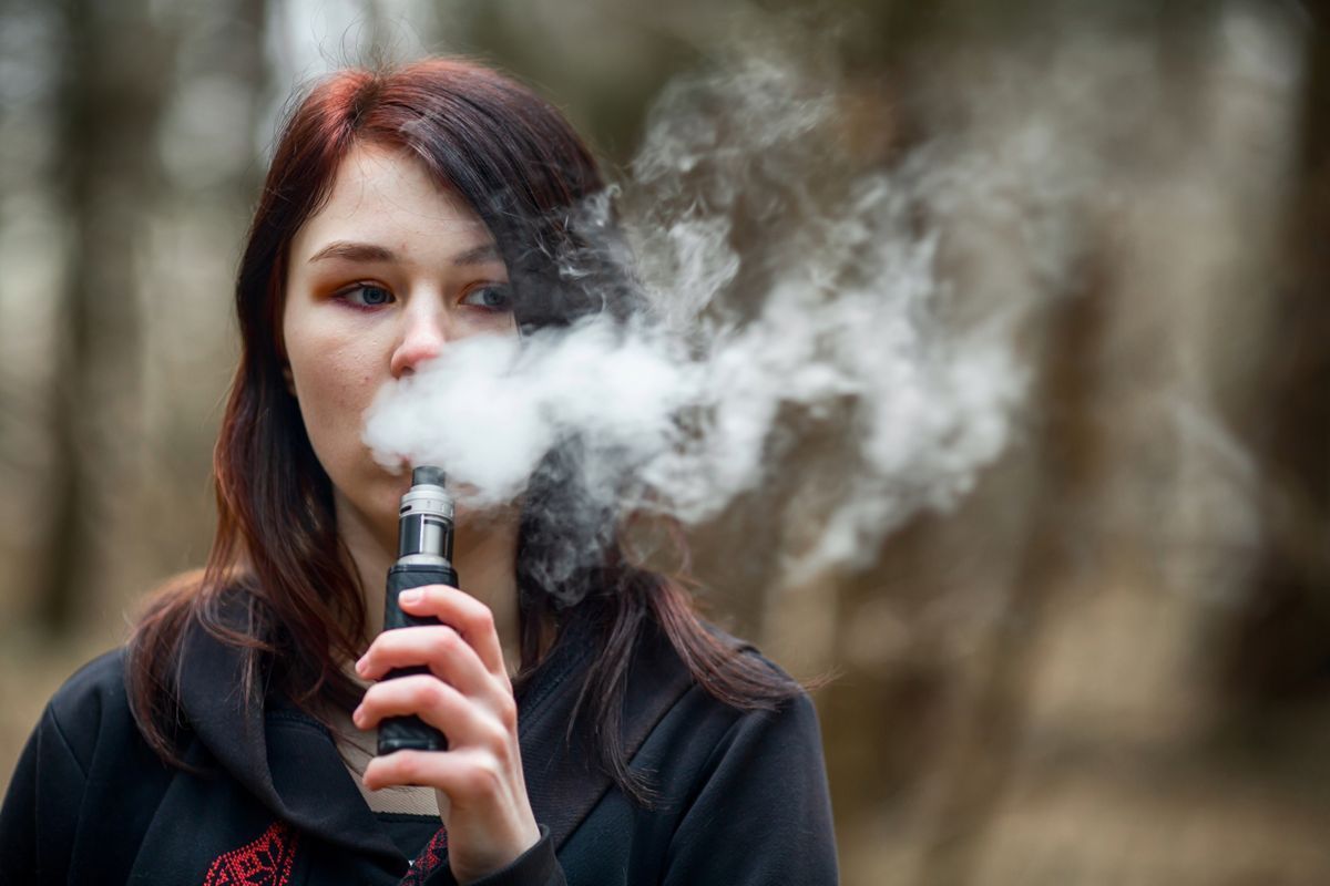 Teenage girl vaping outside, using a vape device and exhaling vapor, highlighting teen vaping awareness and health risks.