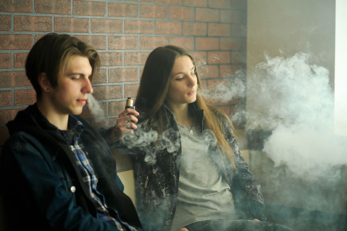 Two teenagers vaping indoors, exhaling vapor, highlighting teen vaping behavior and health risks.
