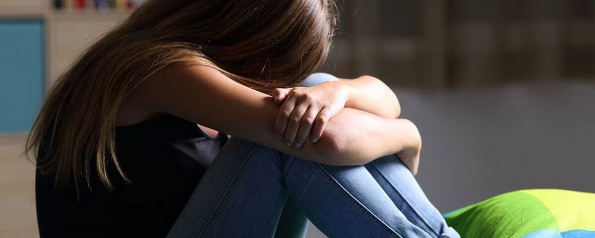Teen girl sitting with head down and arms crossed, showing sadness and emotional struggle during a mental health crisis.