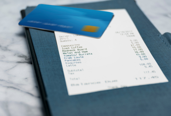 Eine blaue Kreditkarte liegt auf einem Kassenbon, der wiederum auf einer blauen Scheckmappe auf einem Marmortisch liegt.
