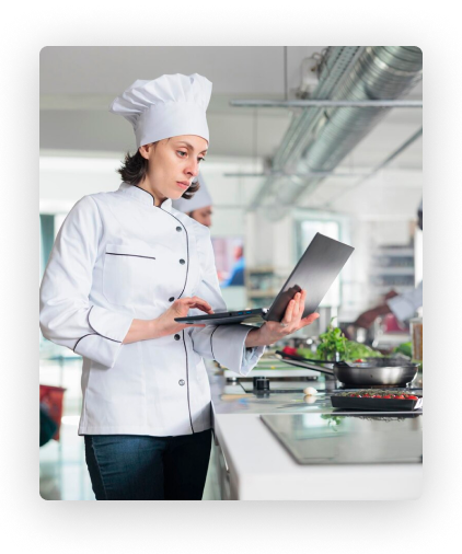 Ein Koch in weißer Uniform benutzt einen Laptop in der Küche.