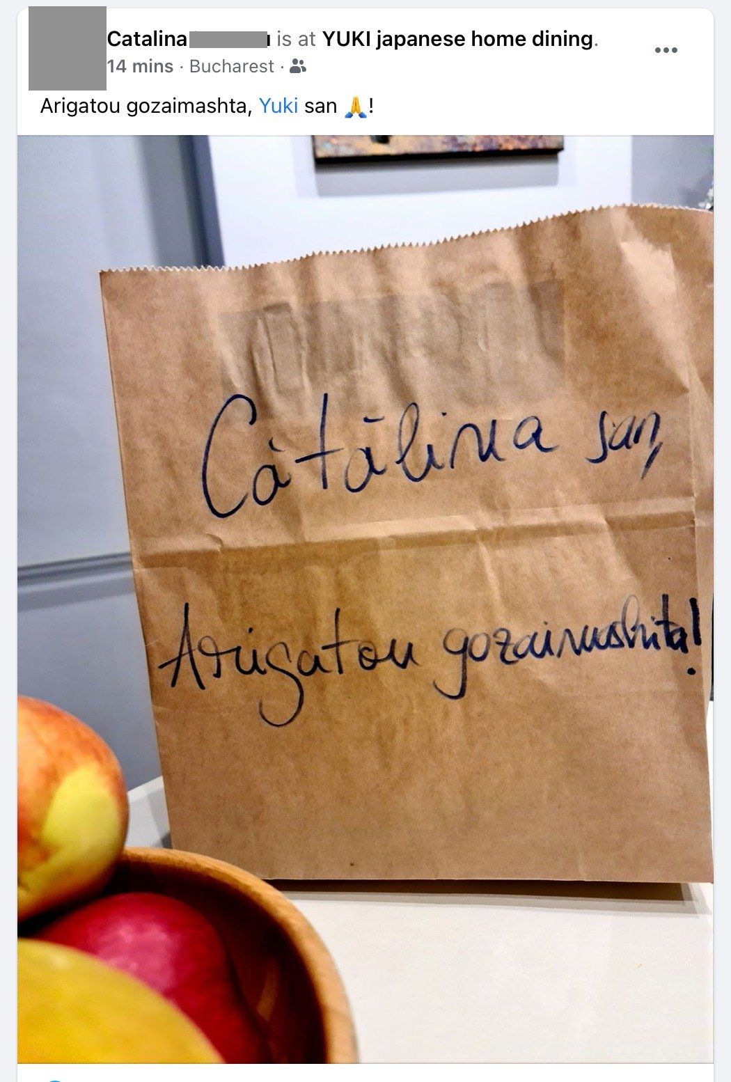 Eine braune Papiertüte mit handgeschriebener Nachricht „Cătălina sun / Arigato gozaimasu!“ neben einer Schale mit Äpfeln.