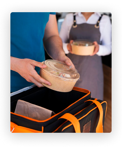 Eine Person stellt einen Lebensmittelbehälter in eine isolierte Liefertasche. Eine andere Person hält einen weiteren Behälter.