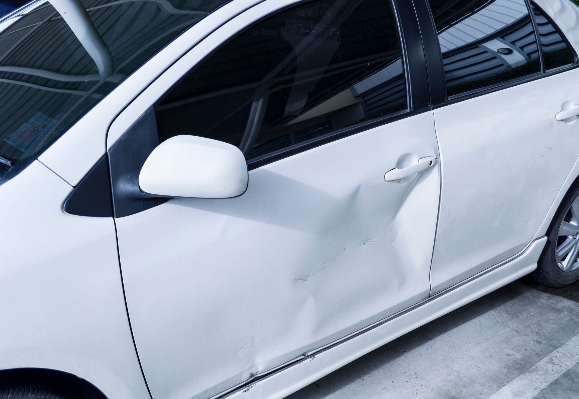A white car with a damaged door is parked in a parking lot.