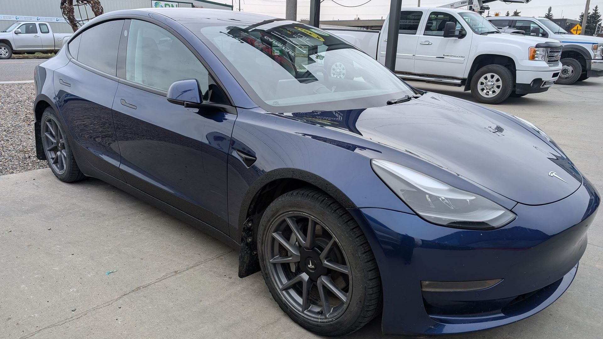 A blue tesla model 3 is parked in a parking lot.
