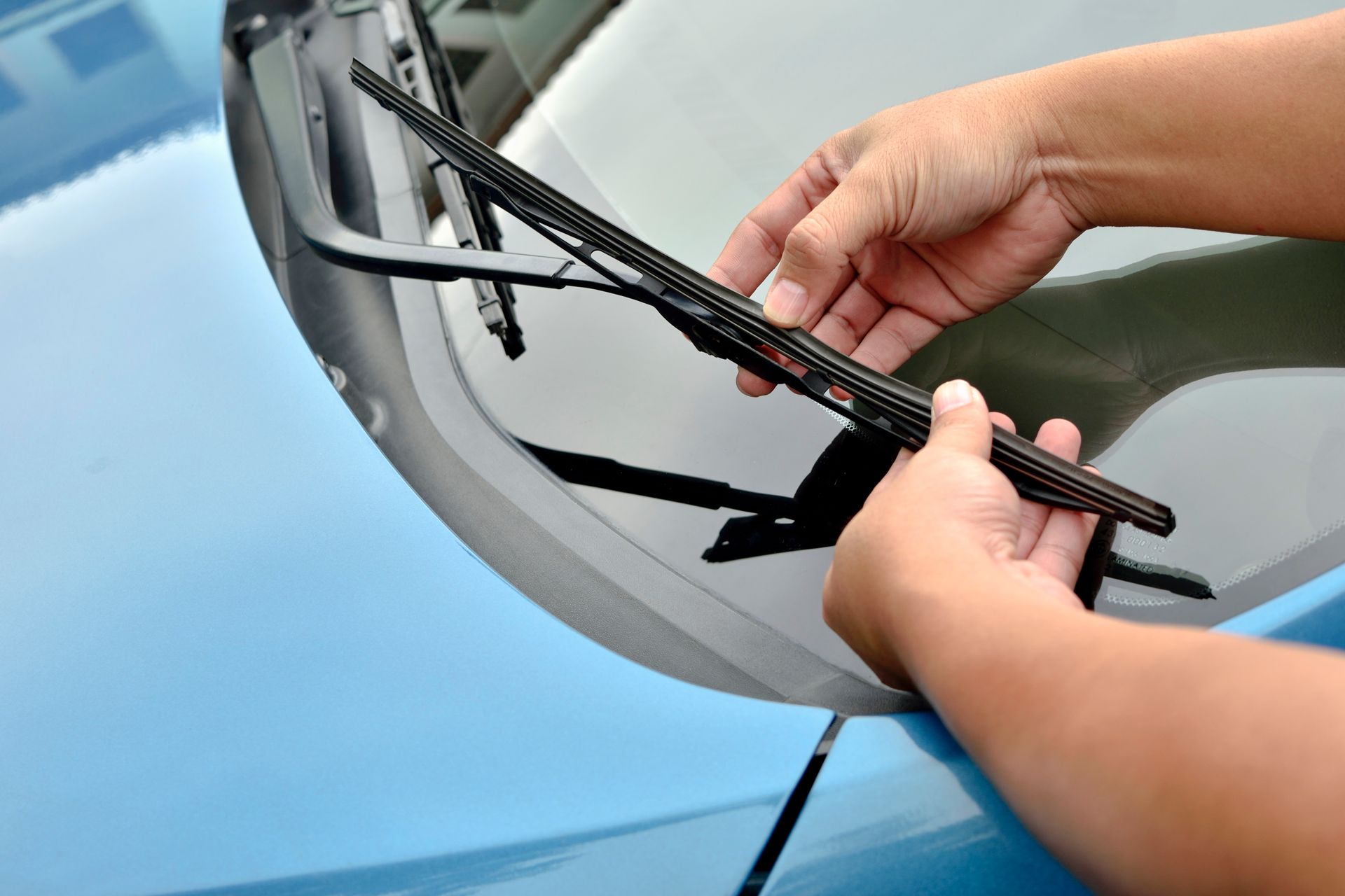 A person is changing a windshield wiper on a blue car.