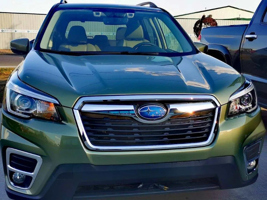 A green subaru forester is parked in a parking lot next to a truck.