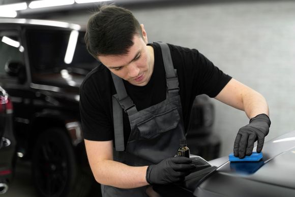 A man is polishing the hood of a car with a sponge.