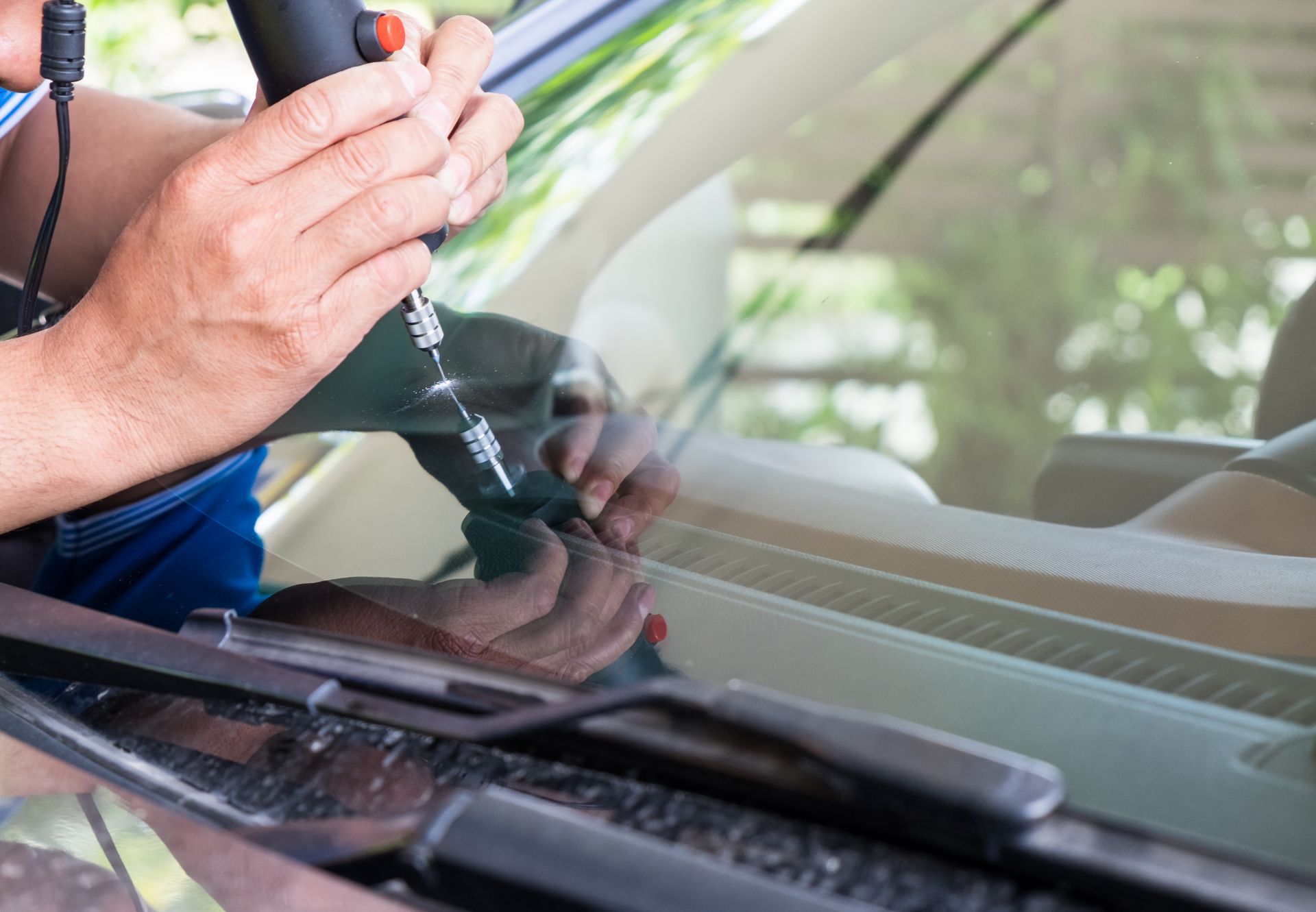 A man is fixing a windshield on a car with a screwdriver.