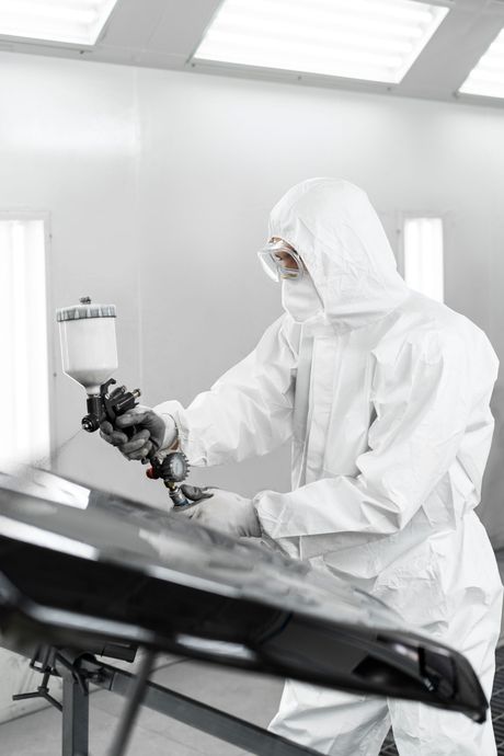 A man in a protective suit is painting a car in a paint booth.