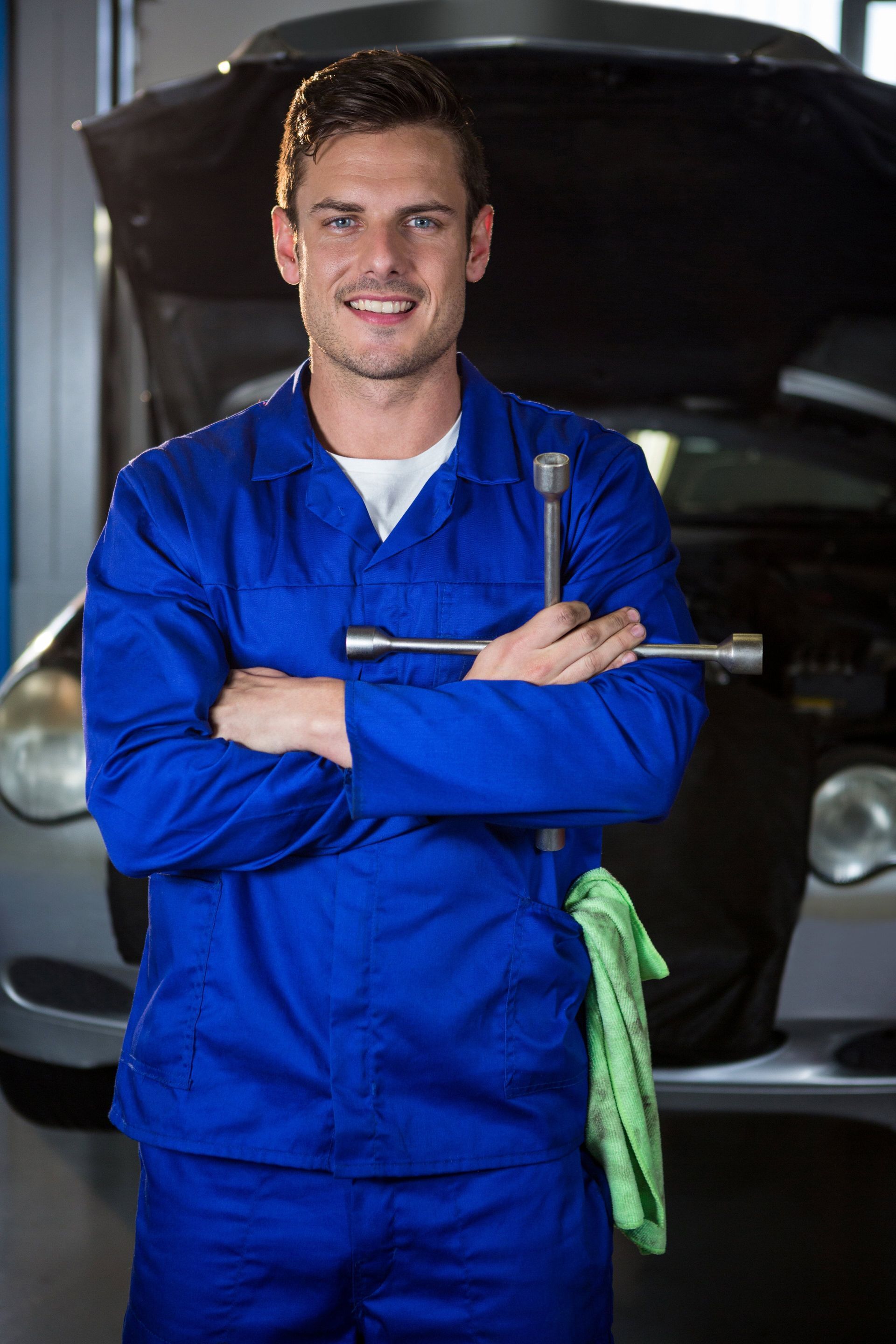 A mechanic is holding a wrench in front of a car in a garage.