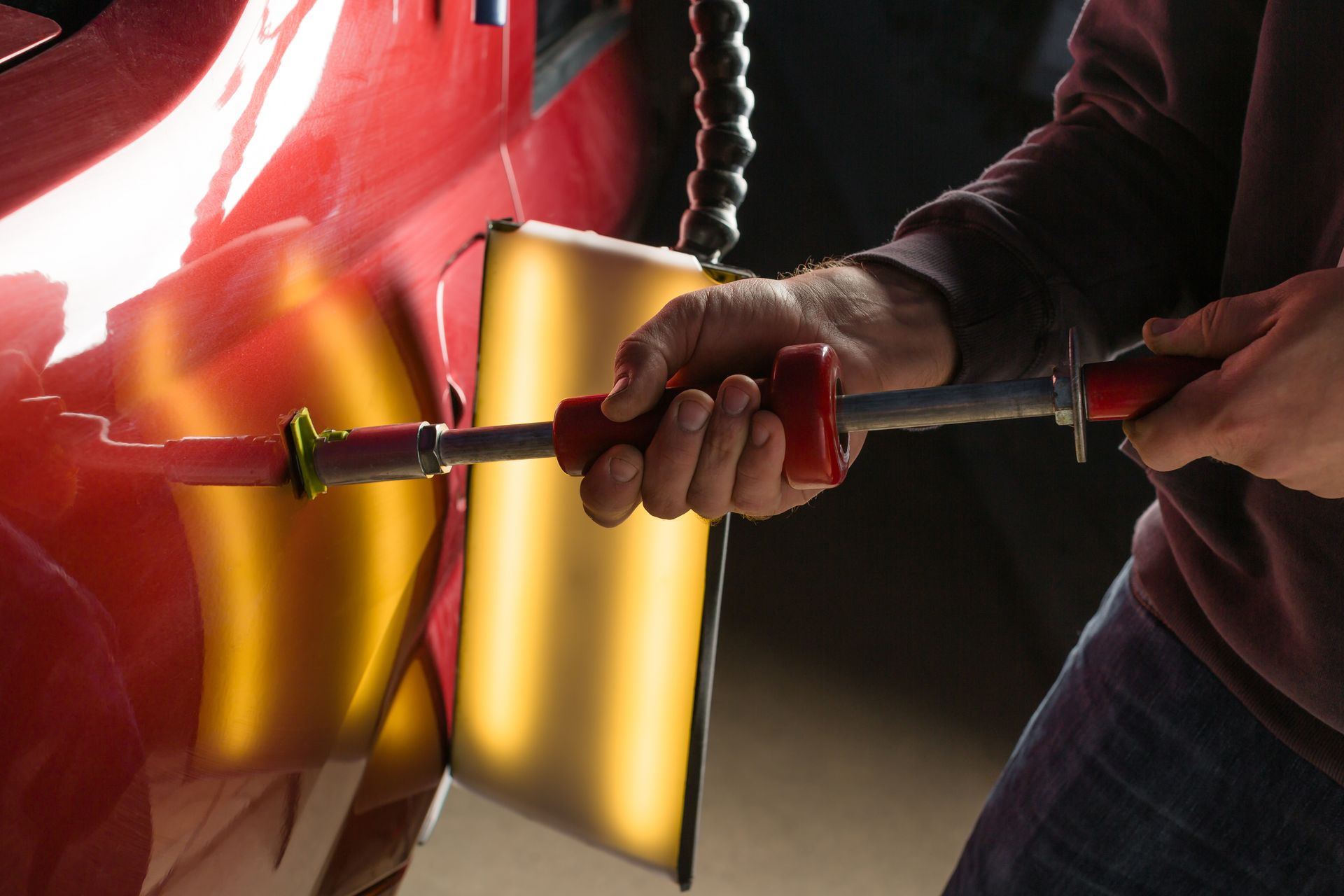 A person is working on a red car with a tool