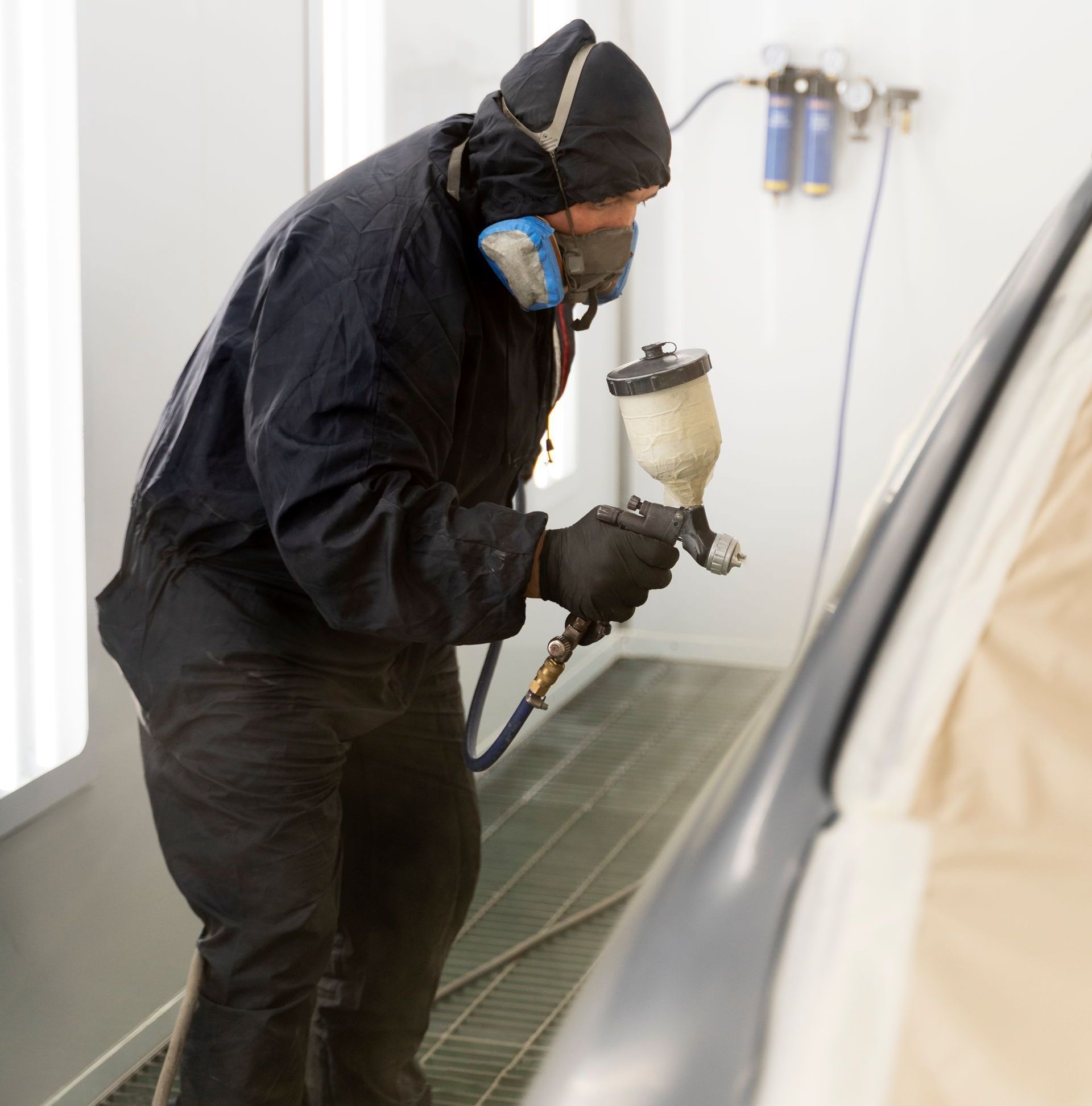 A man wearing a mask is spray painting a car