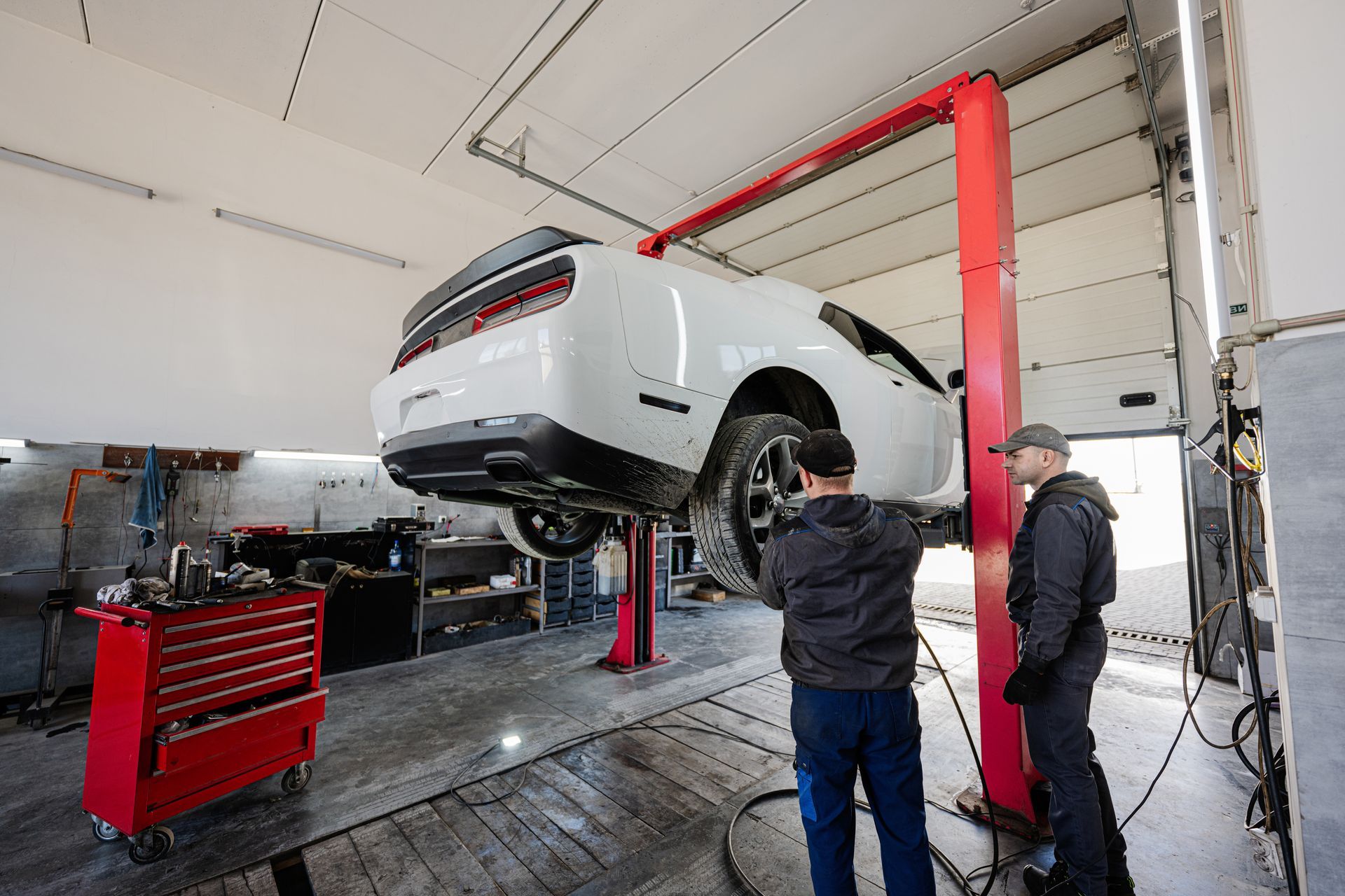 Two men are working on a car on a lift in a garage.