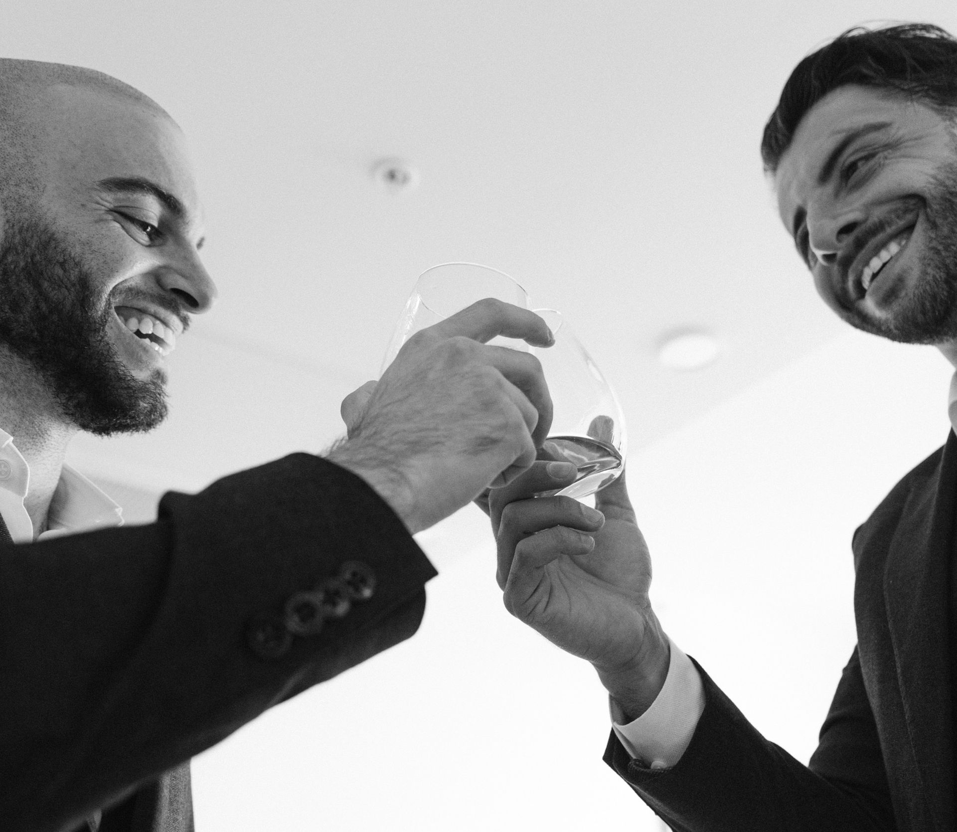 Two men in suits toasting glasses, smiling.