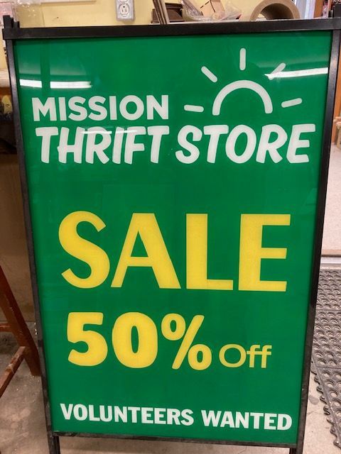 A green sign that says mission thrift store sale 50 % off