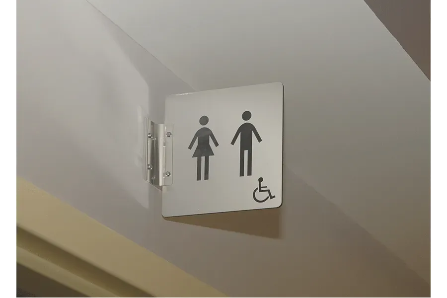 A stainless steel toilet sign with a handicapped symbol on it.