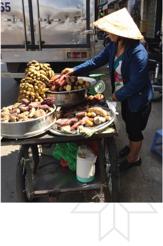 A woman is standing in front of a cart selling food.