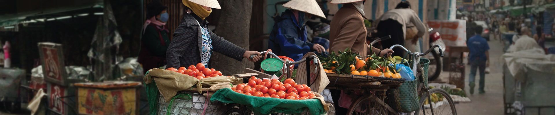 A group of people are standing on a sidewalk selling fruit and vegetables.