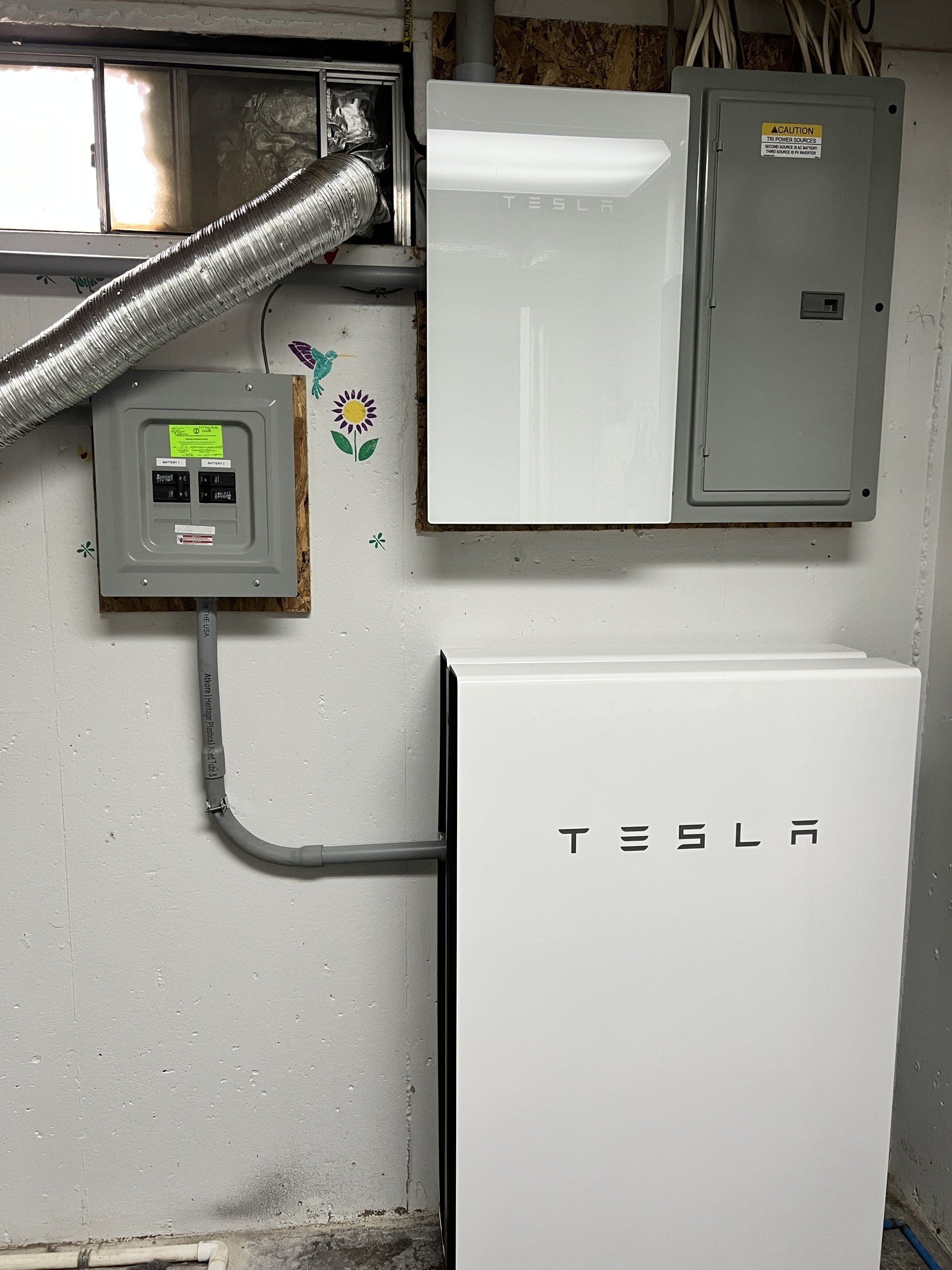 A tesla battery is sitting on a wall next to a electrical box.
