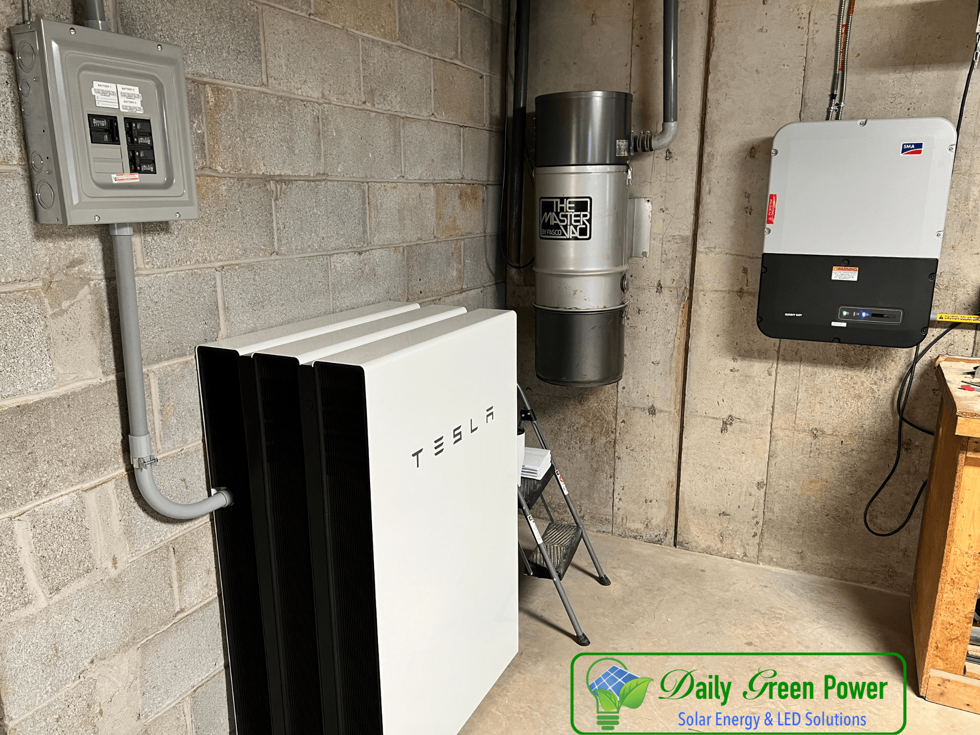 A tesla battery is sitting in a basement next to a vacuum cleaner.