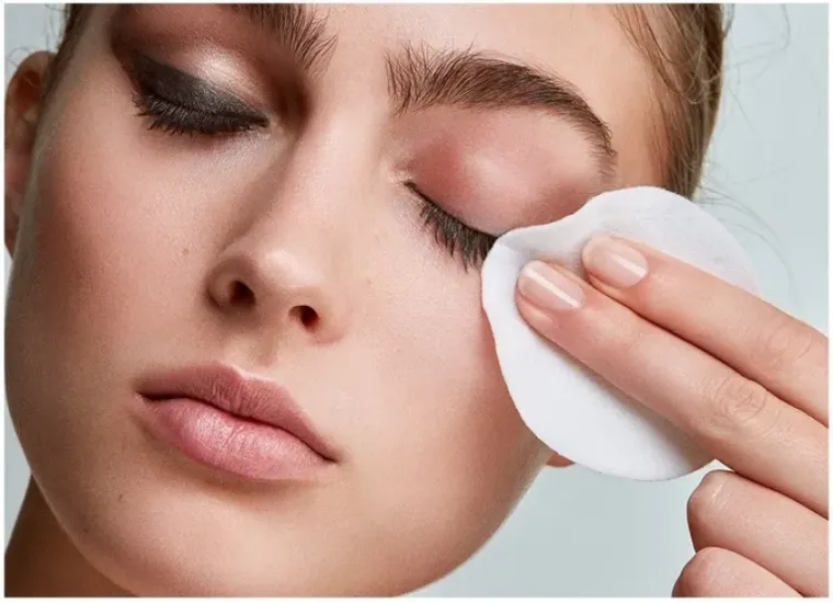 A woman is cleaning her face with a cotton pad.