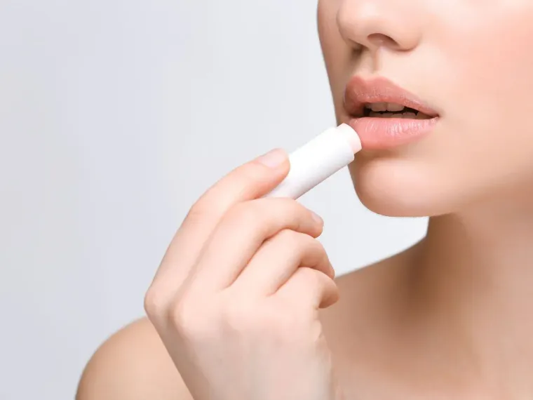 A woman is applying lip balm to her lips.