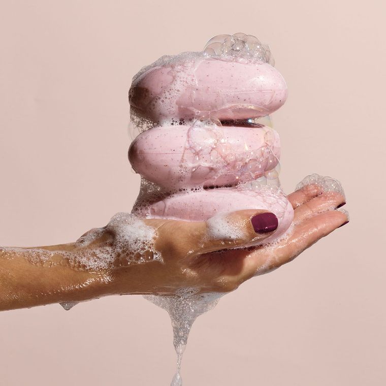 A woman is holding a stack of pink soap bars in her hand.