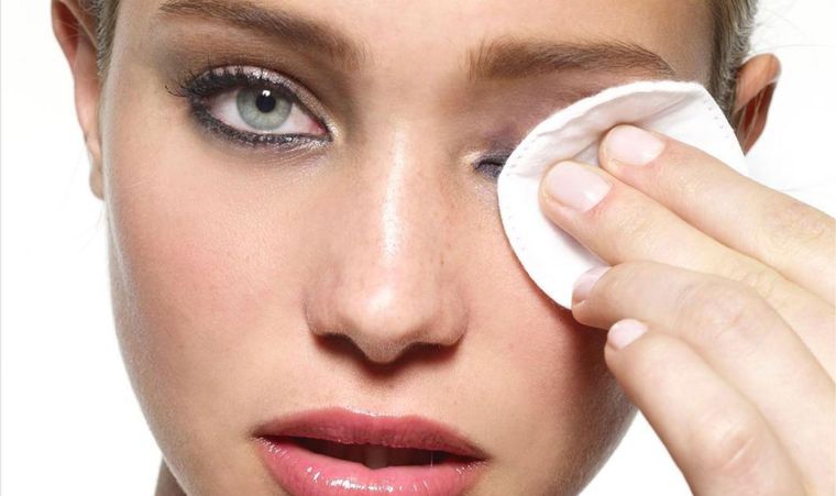 A woman is cleaning her eye with a cotton pad.