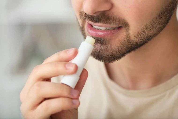 A man with a beard is applying lip balm to his lips.