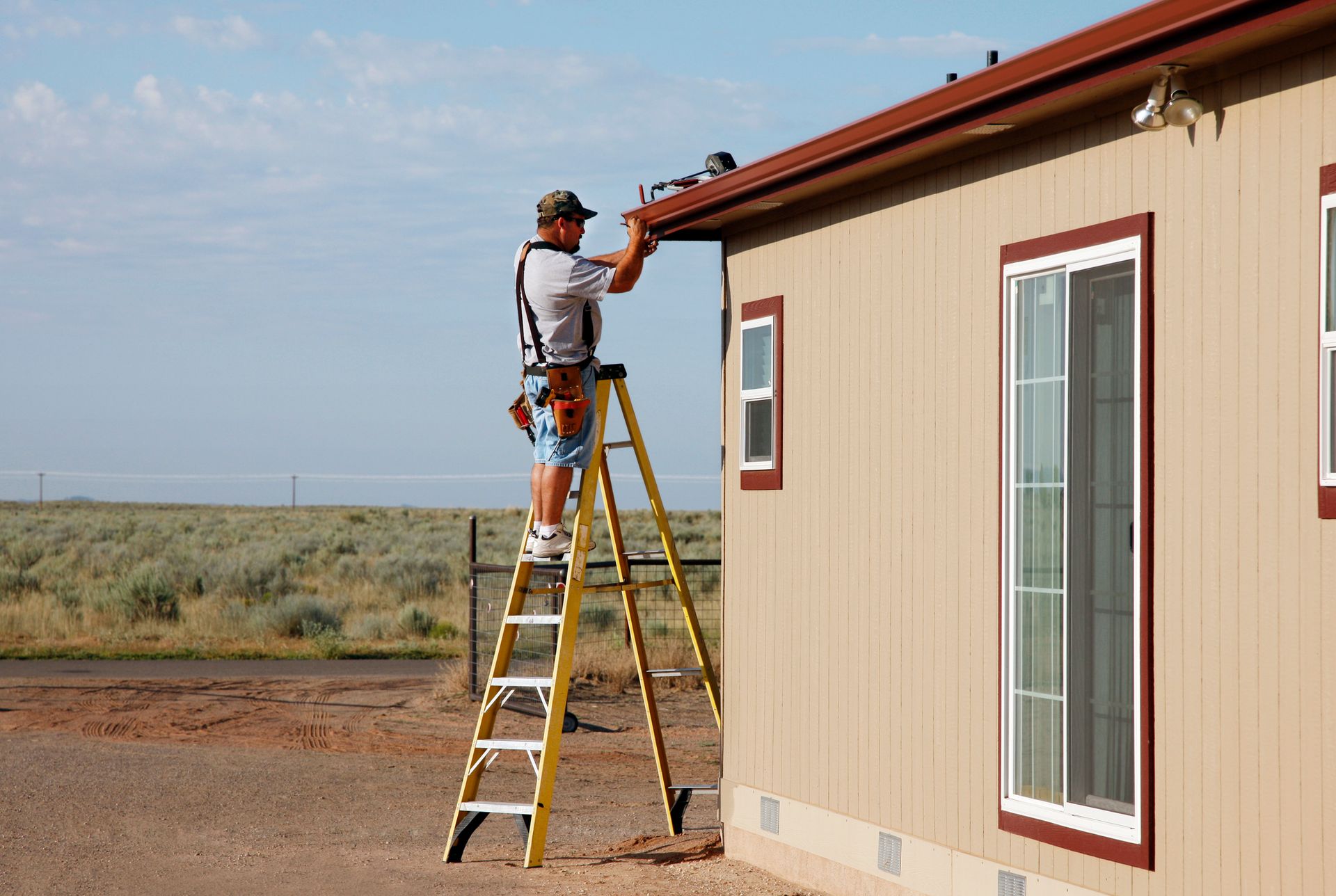 A male worker on a ladder is performing seamless gutter installation, on a residential home.