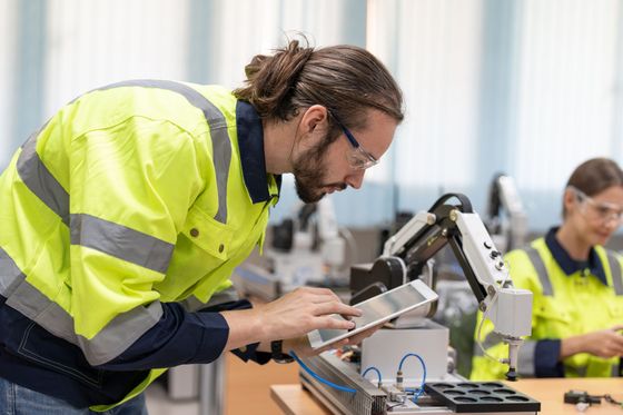 Ein Mann arbeitet an einem Roboterarm und schaut dabei auf ein Tablet.