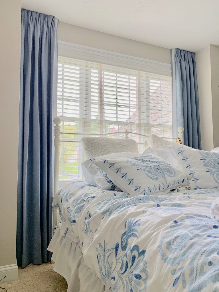 a bedroom with a bed , curtains and shutters Simply Windows.