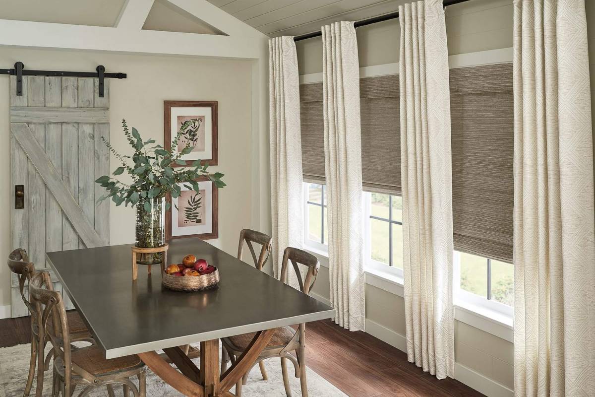 a dining room with a table and chairs and windows with woven wood shades and draperies Simply Windows.