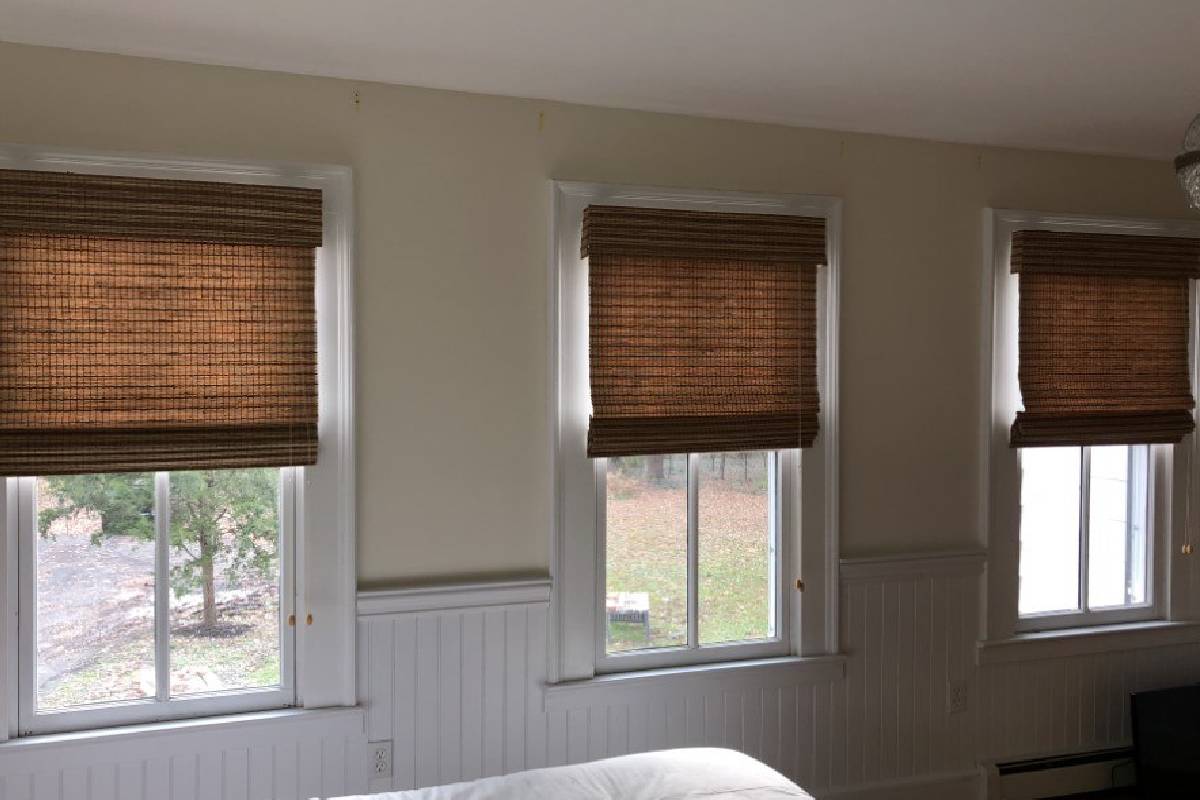 a bedroom with a bed and three windows with woven wood shaded on them Simply Windows