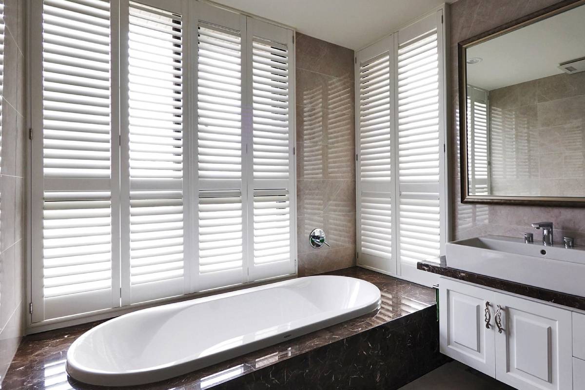 a bathroom with a tub , sink , mirror and shutters on the windows Simply Windows.