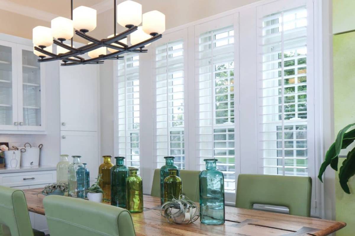 a dining room with a table and chairs and a chandelier and shutters on the windows Simply Windows