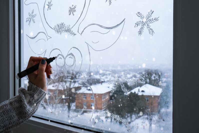 10 Tips for Christmas Window Decorations: A woman draws with window paint.
