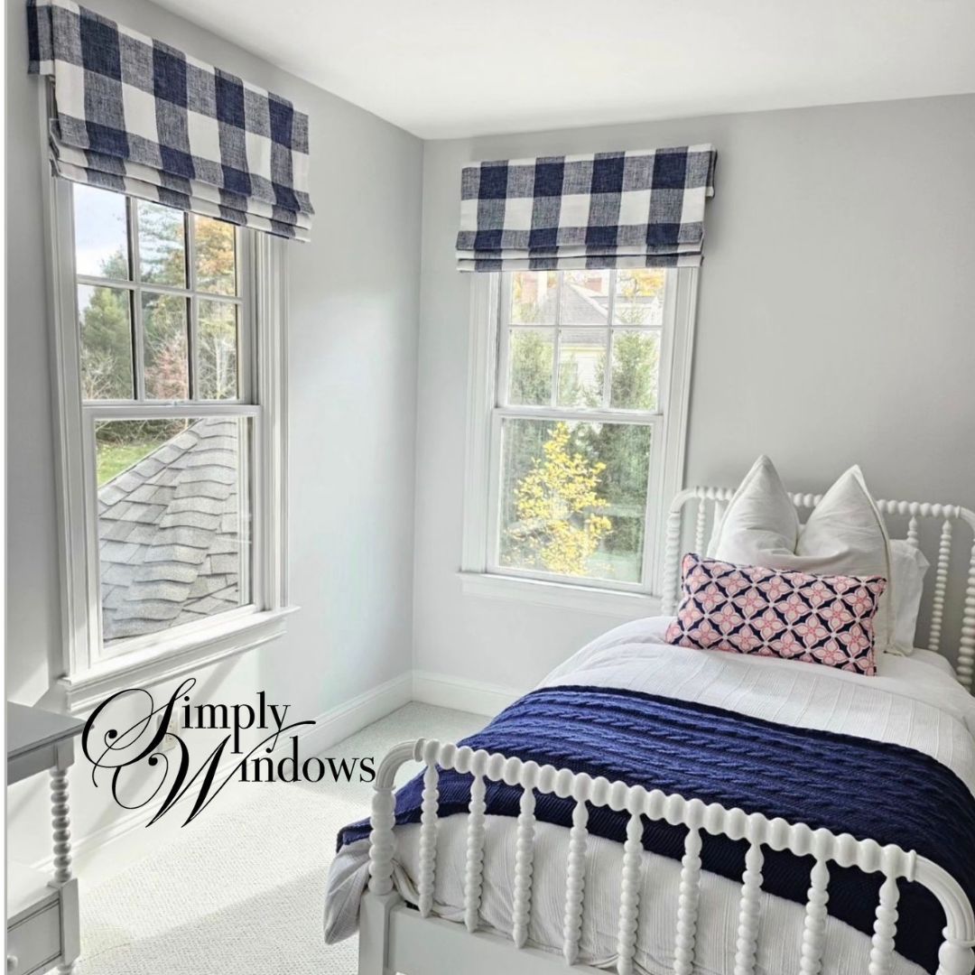 Small bedroom with plaid faux roman shades, white bed, blue blanket, and bright windows.