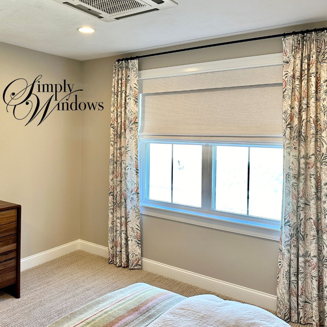 Bright bedroom with a window, beige walls, patterned curtains, and a Roman shade.